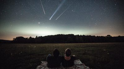 Ночное небо с россыпью падающих звёзд над тёмным летним полем