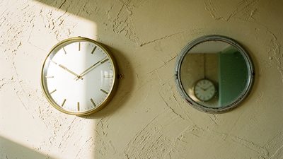 Старые настенные часы со стрелками на 10:10 и их отражение в круглом зеркале на светлой стене