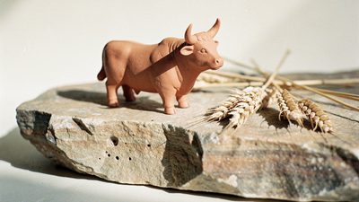 Маленькая терракотовая фигурка быка на каменной плите рядом с сухими колосьями в утреннем свете