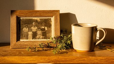 Семейное фото в деревянной рамке, керамическая кружка и летние травы на полке в тёплом свете солнцестояния
