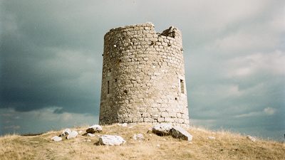 Старая каменная башня на сухом склоне под широким спокойным небом с расходящимися тучами
