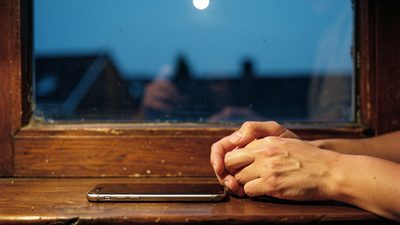 Девушка пишет сообщение в телефоне у окна с весенними цветами — лёгкое окно общения под Венерой в Близнецах