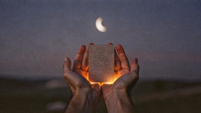 Женщина у окна на закате со свечой, на столе колода Таро и весенняя зелень в вазе
