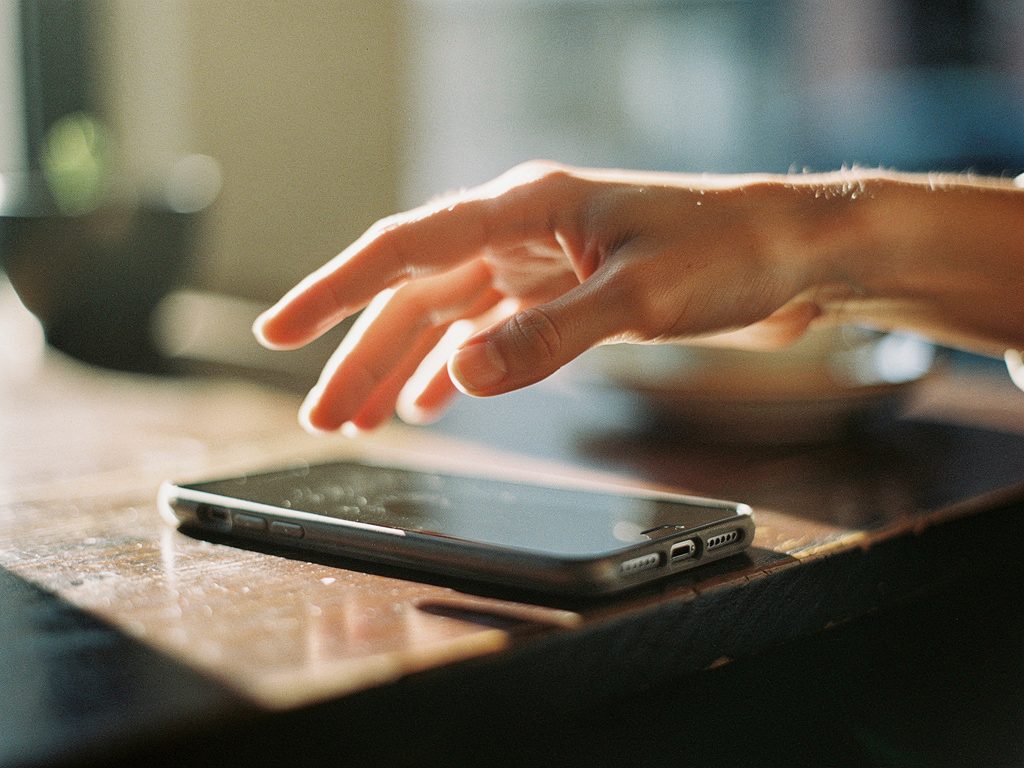 Женская рука над смартфоном на деревянном столе в тёплом свете