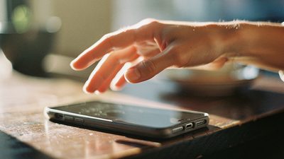Женская рука над смартфоном на деревянном столе в тёплом свете