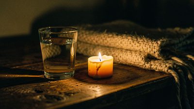 Стакан воды и зажжённая свеча на деревянном столе тёплым вечером новолуния