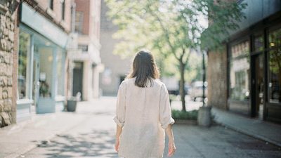 Молодая женщина в кафе европейского города смотрит на телефон с лёгкой улыбкой, рядом блокнот и чашка